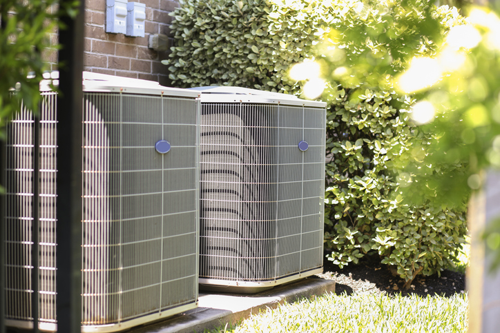 Air conditioner unit outdoors in side yard of a brick home in hot summer season