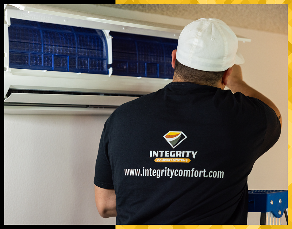An Integrity HVAC technician facing away from the camera, examining a ductless HVAC system